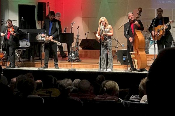 A band performs on stage with various instruments in front of an audience at a venue labeled 