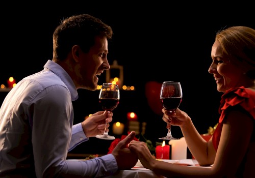 A couple enjoying a romantic candlelit dinner, holding glasses of red wine and smiling at each other.