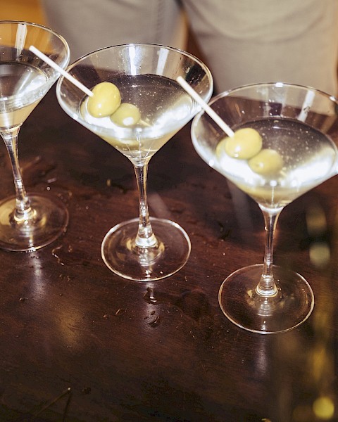 Five martini glasses with olives on a dark surface, ready for serving.