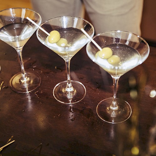 Five martini glasses with olives on a dark surface, ready for serving.