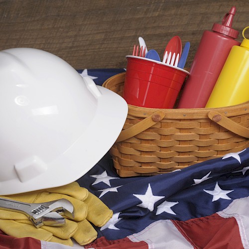 A white hard hat, wrench, gloves, basket with condiments, and utensils on an American flag-themed cloth.