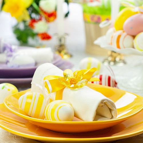 A festive table setting with decorated Easter eggs, napkins, and flowers on colorful plates, perfect for a spring celebration.