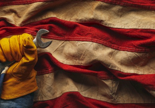 A gloved hand holding wrenches emerges from a wrinkled American flag, symbolizing labor and patriotism.