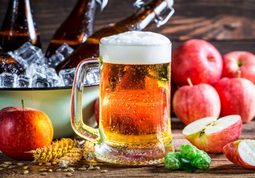 A glass of beer with a foamy head, bottles in ice, apples, wheat, and hops arranged on a wooden surface complete the scene.