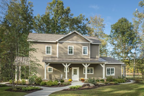 A two-story house with a porch, surrounded by a landscaped yard and trees under a clear, blue sky. A curved pathway leads to the entrance.