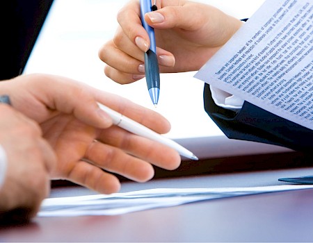 Two people exchanging pens while reviewing documents, suggesting a business or legal agreement context.