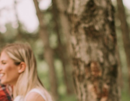 Four people are walking through a forest; they appear to be hiking, with one person smiling at the camera and carrying a backpack, ending the sentence.